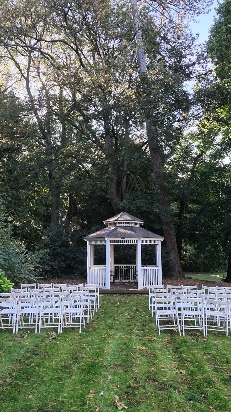 Outdoor ceremony aisle leading to a gazebo under tall trees