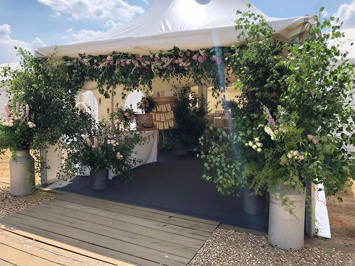 Marquee entrance dressed with greenery, pink flowers and milk churns